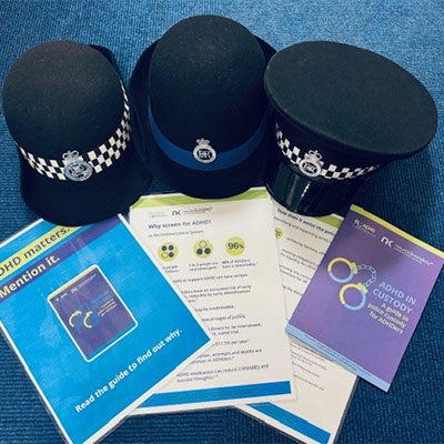 Various printed neurodiversikey resources laid out next to three police hats.