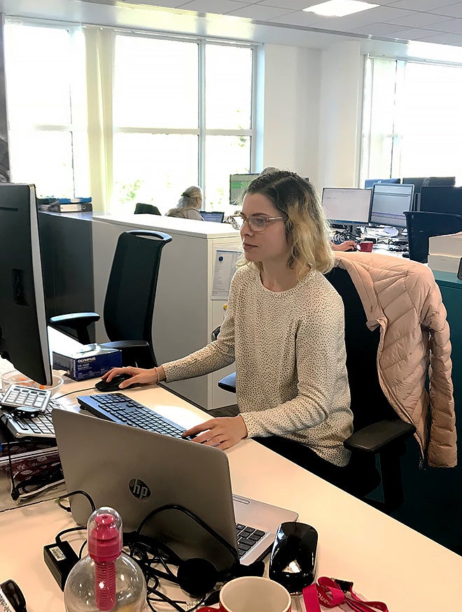 A smiling young woman working on a computer at her desk in an open-plan office