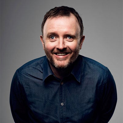 Chris McCausland smiling at the camera. He has short brown hair and is wearing a navy shirt.