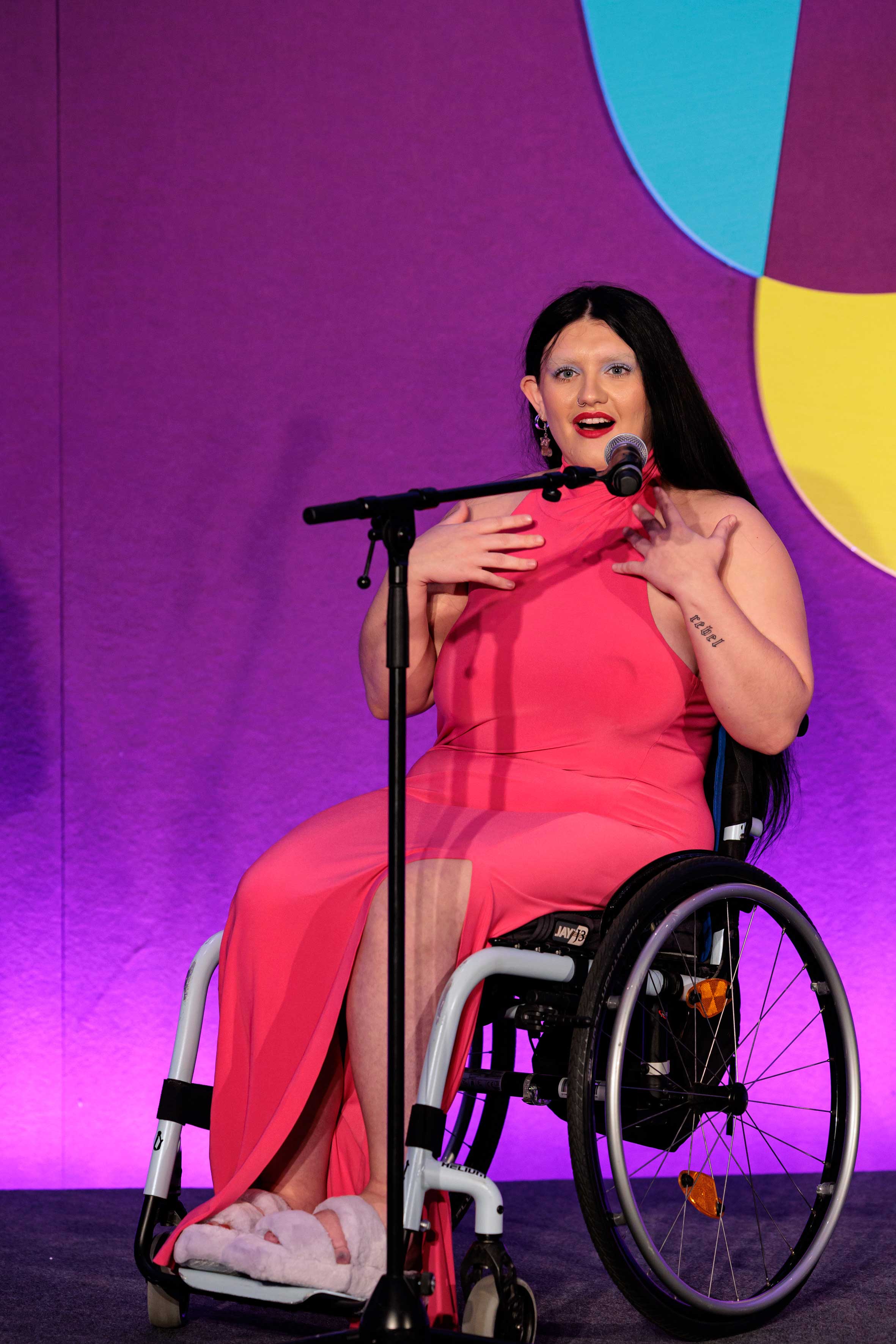 A woman in a pink dress in a wheelchair with a microphone