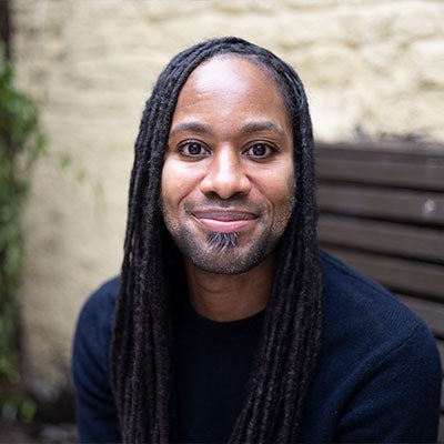 A photo of Jason Arday smiling. He has long dreadlocks and wears a black jumper.