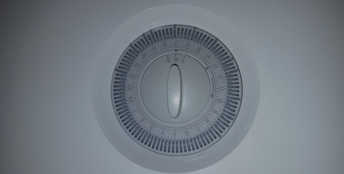 Mechanical heating controls. There is a dial with on, off and hour markings. There are switches around the dial arranged in a circle, one for each hour of the day. 