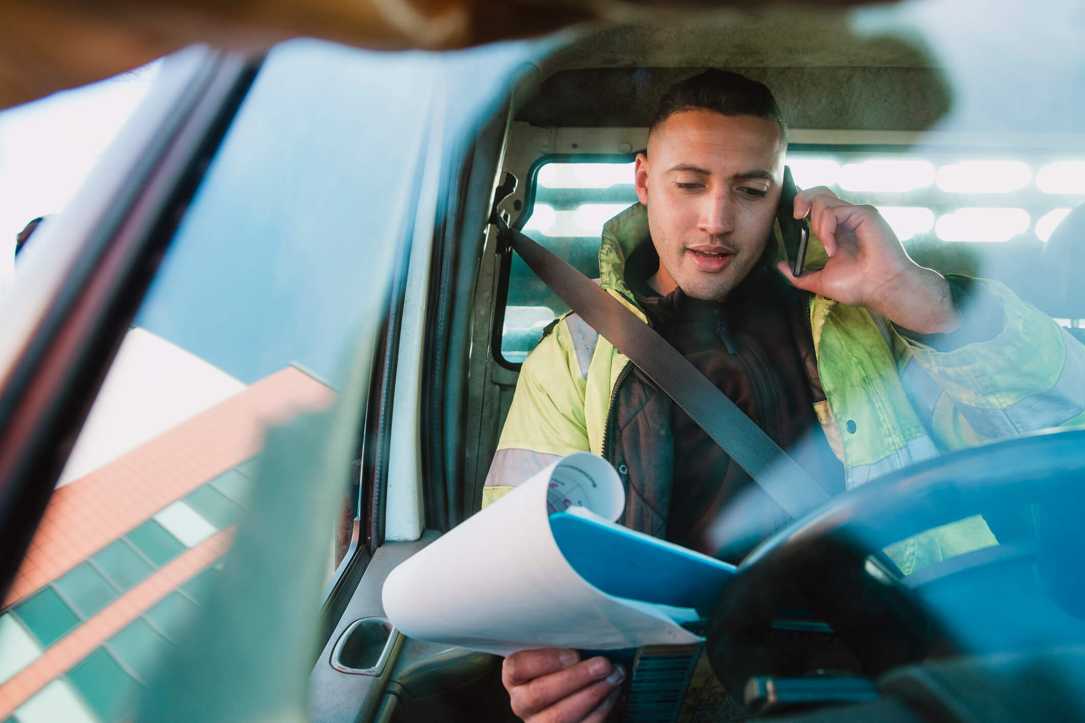 Tradesman sat in a van, on the phone and holding a clipboard