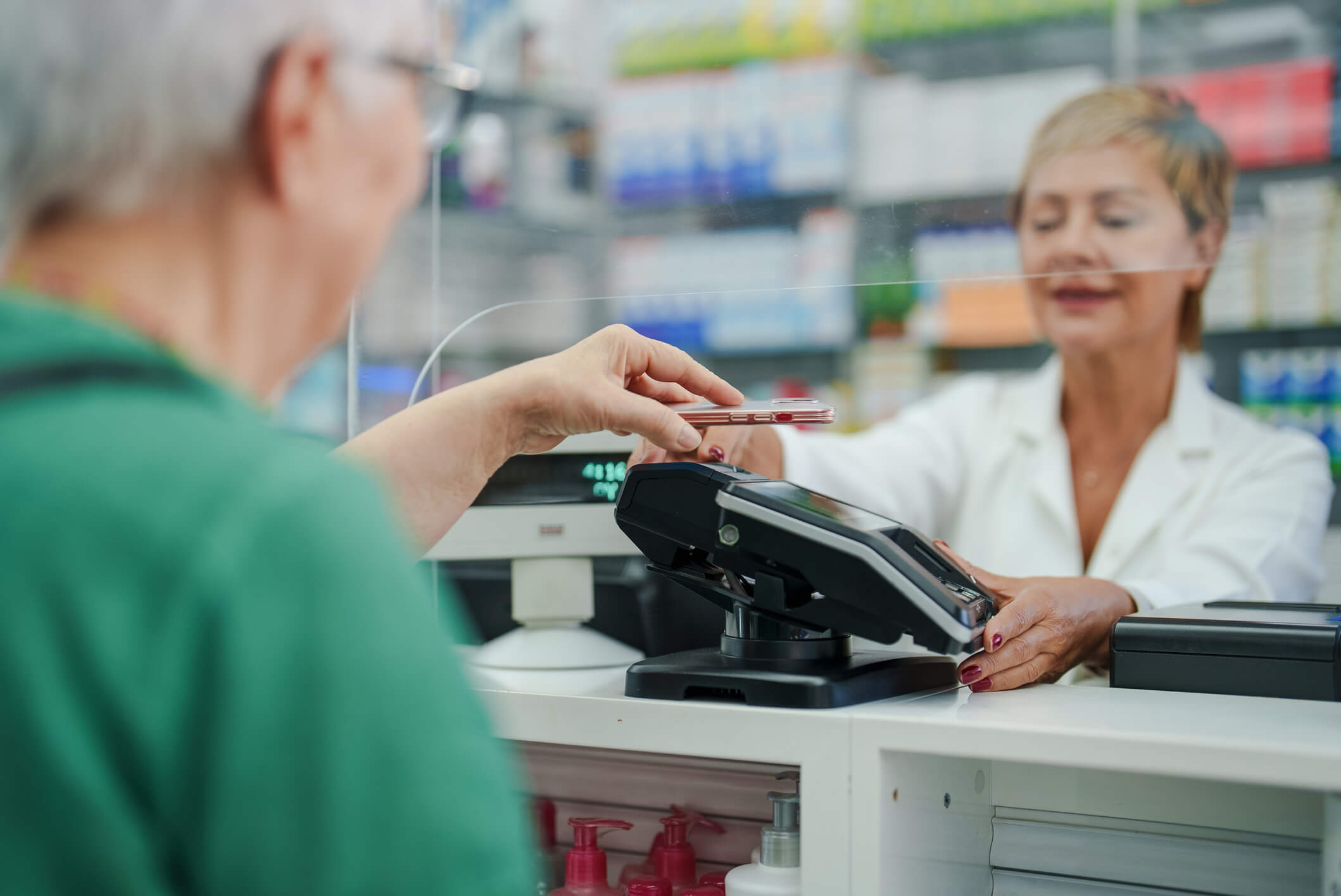 Senior woman using her smartphone to pay for medicines at pharmacy checkout