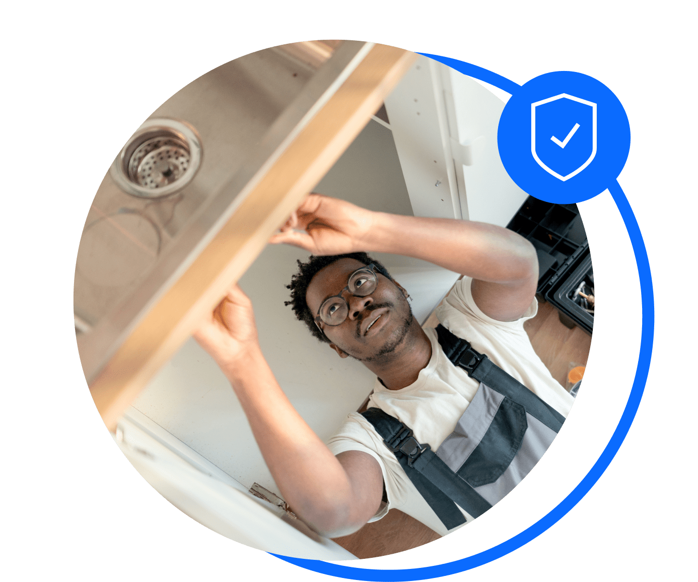 A plumber in blue opveralls lies underneath a sink. He's thinking about sorting his trades insurance.