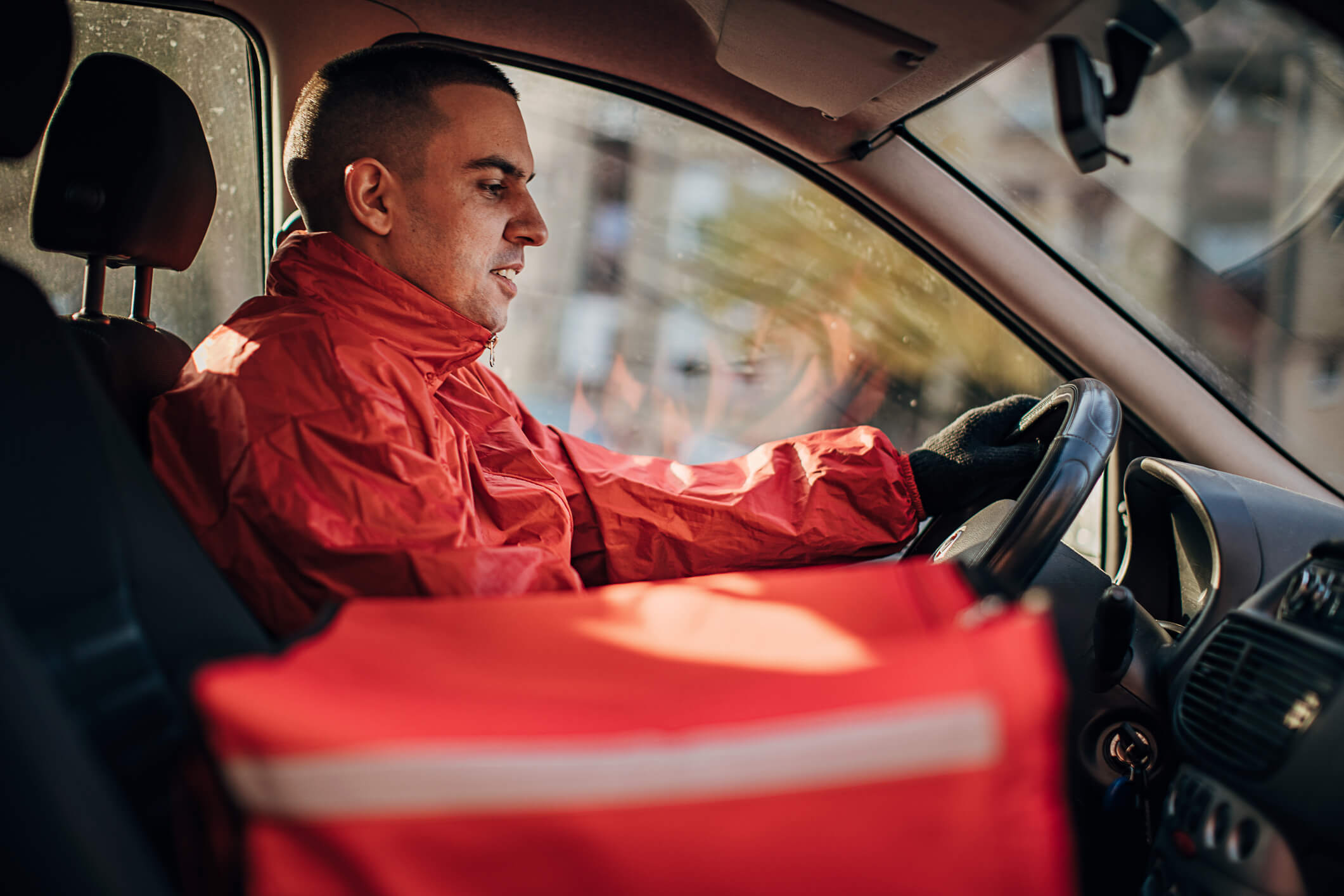 Male delivery driver sat in the driving seat of a car with a food delivery on the next seat