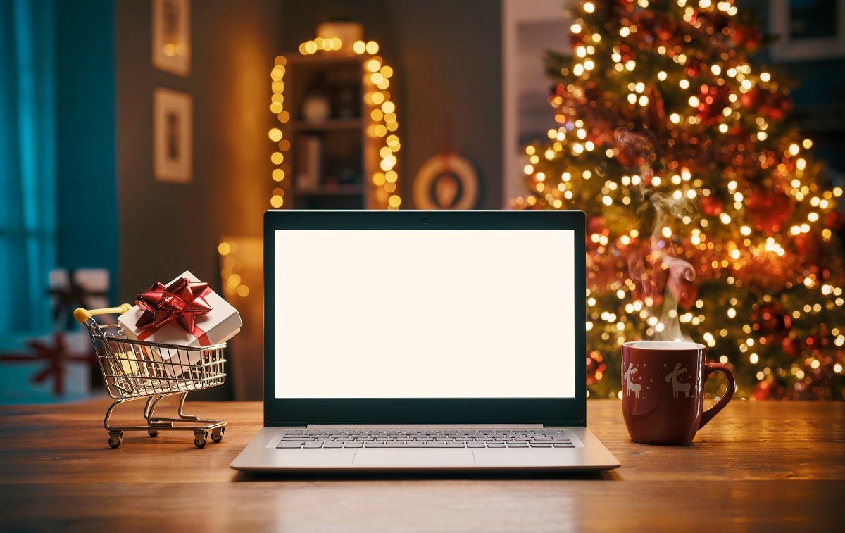 An open laptop in front of a Christmas tree decorated with twinkling lights