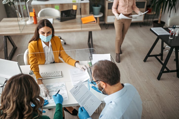 Couple of business owners signing a coronavirus loan document in a meeting at bank all are wearing protective gloves and face masks