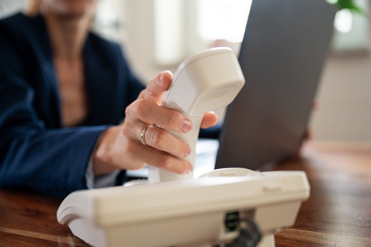 female picking a phone receiver from a handset on a desk