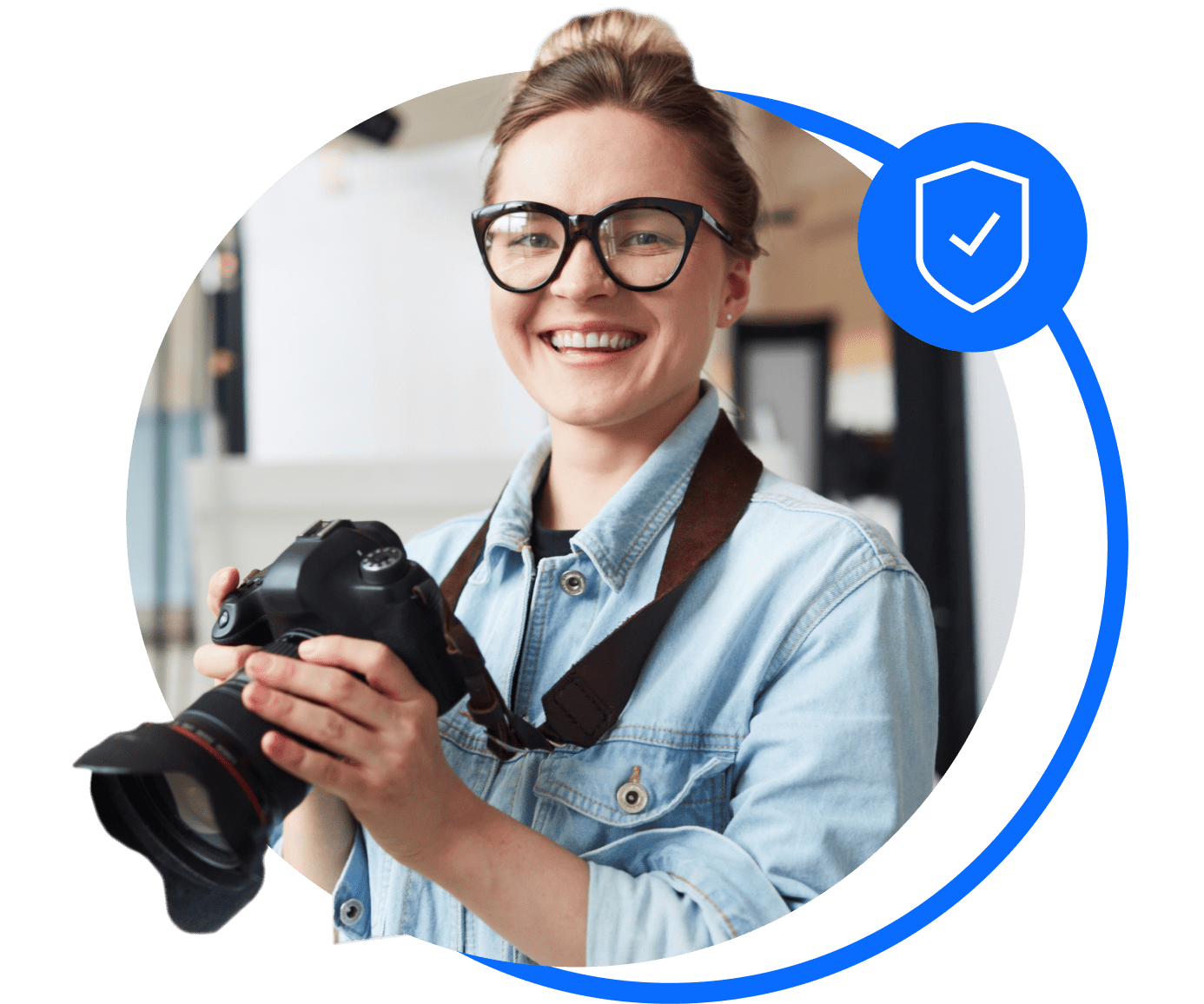 A photographer in a blue shirt and glasses holds her camera and smiles after sorting her professional and trades insurance.