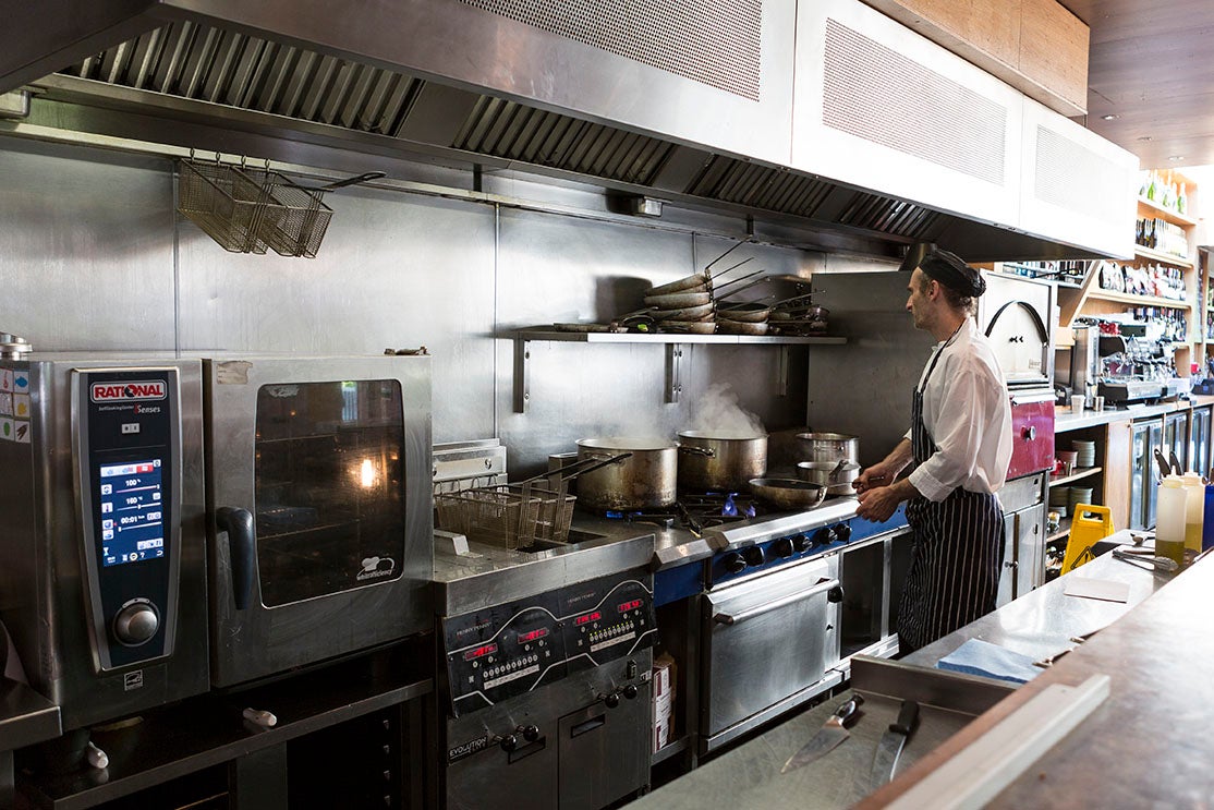 A chef cooks using pan on a commercial cooking range