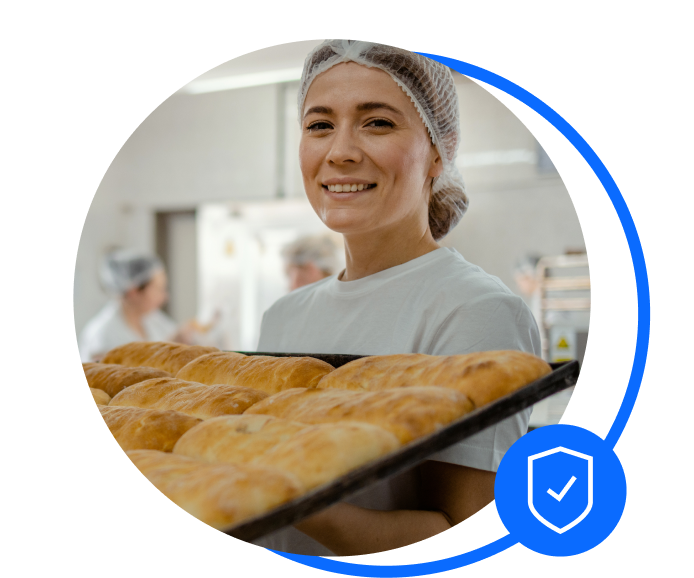 A baker holding a tray of baked goods. She's smiling after sorting her business insurance.
