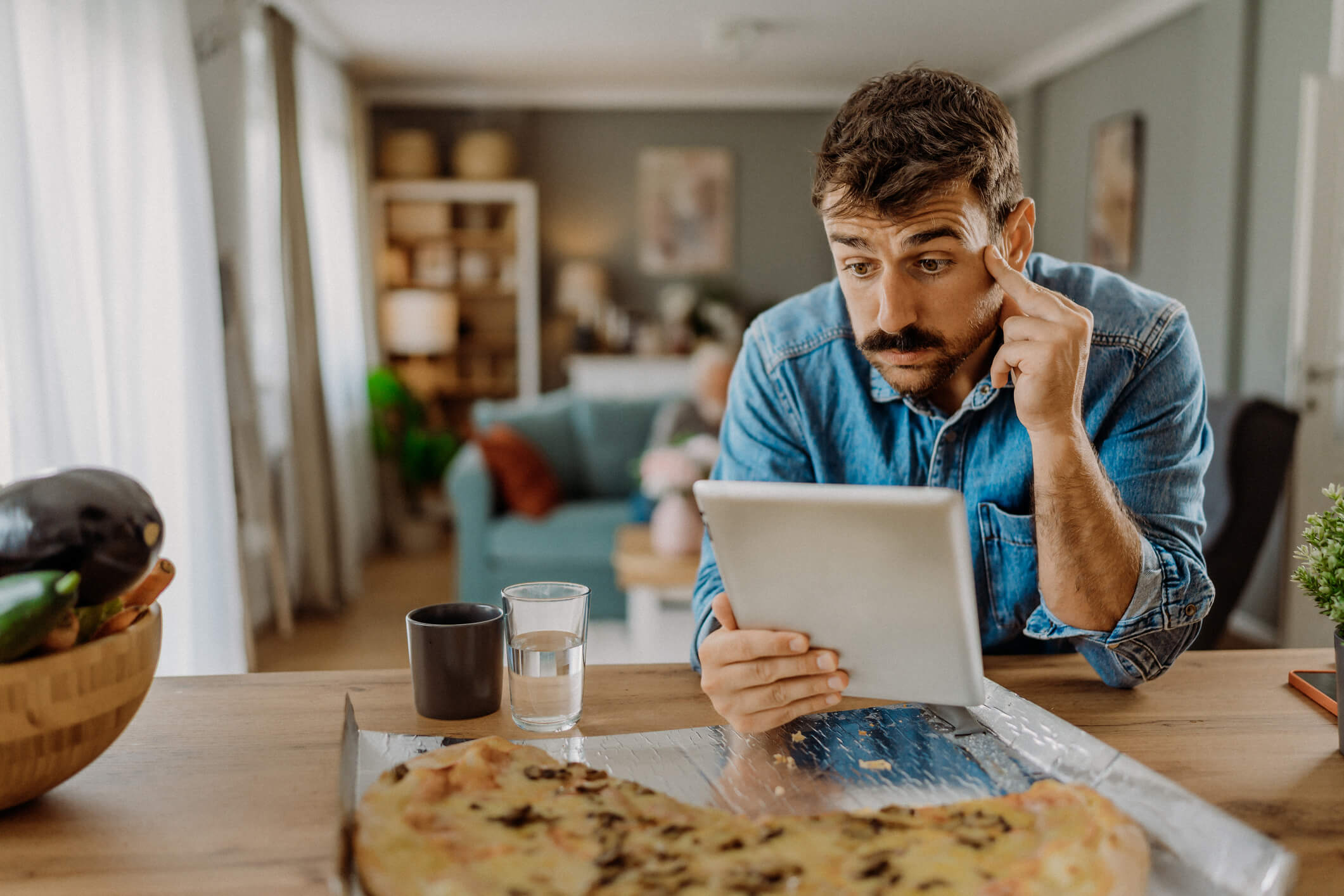 Male  in his house sat using a iPad looking confused