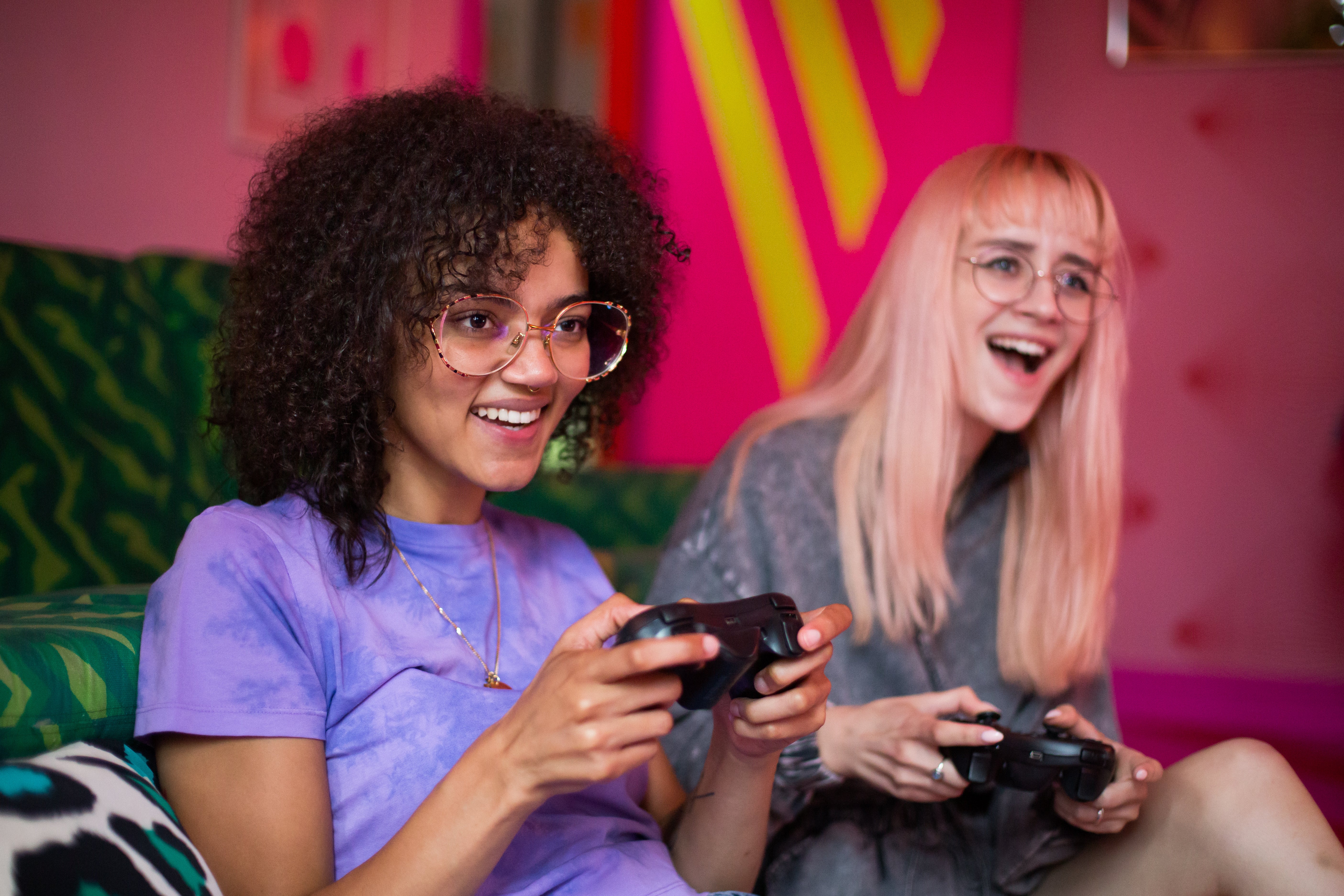 Two women sitting on a green couch concentrating on playing a game