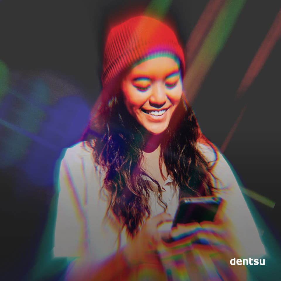 A woman in a red hat with long brown hair looking at her phone in front of a dark background with a aurora-esque shards of light