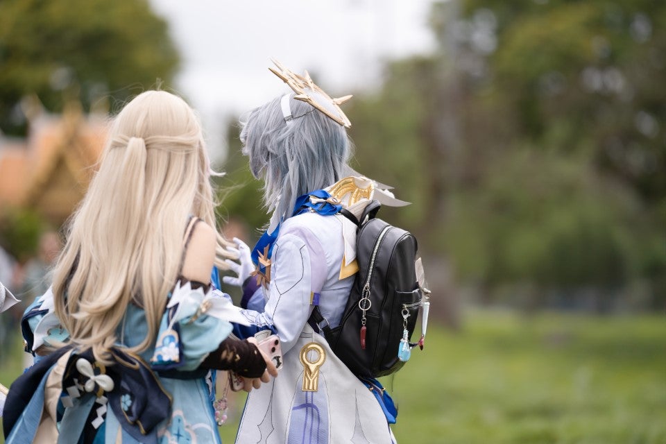 Two Cosplayers dressed in white facing away from the camera with a blurred green background