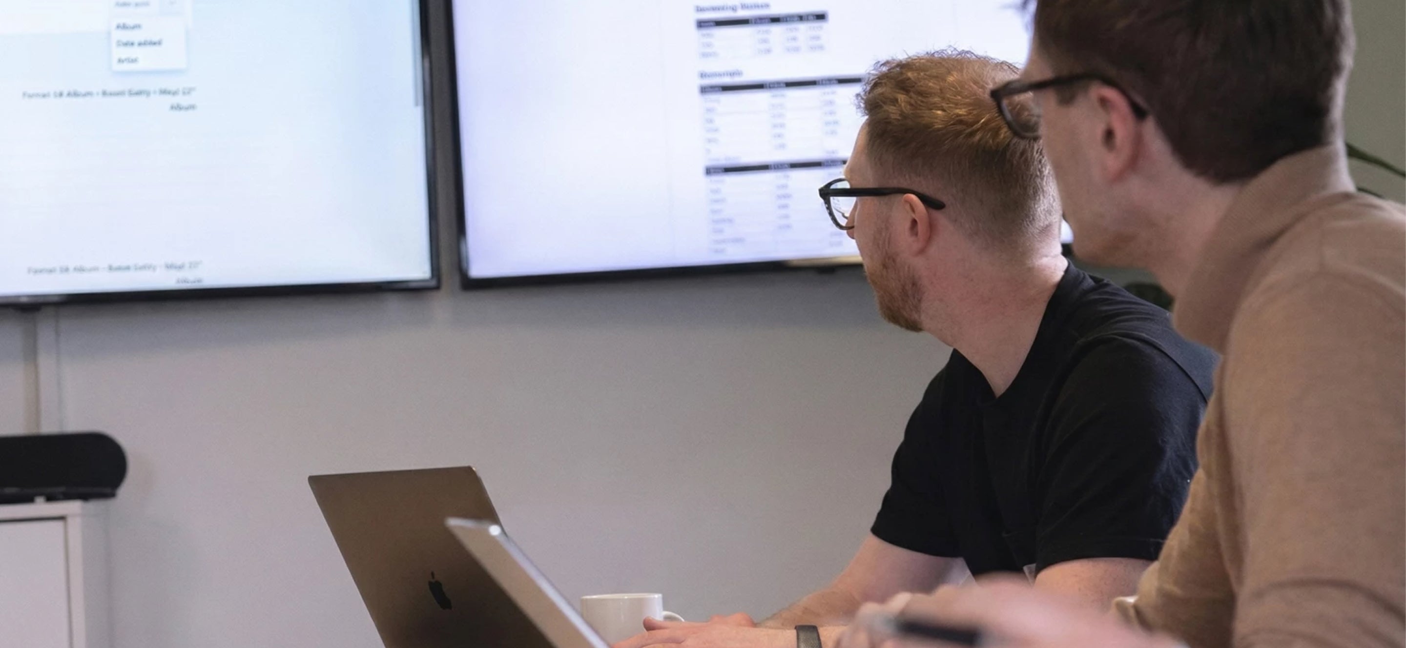 Two men in a meeting room looking at info on a large screen.