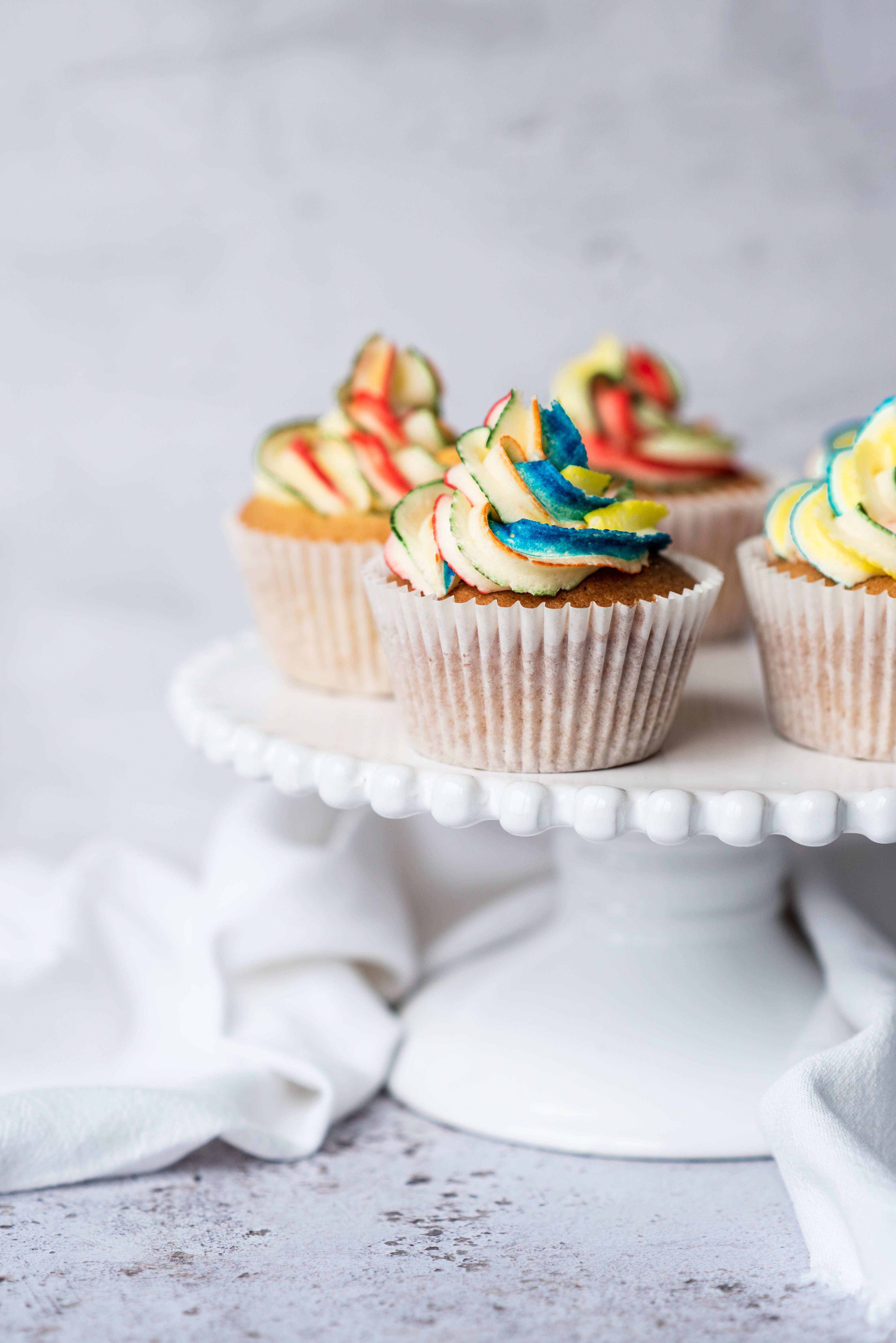 rainbow buttercream on a cupcake sitting on a cake stand