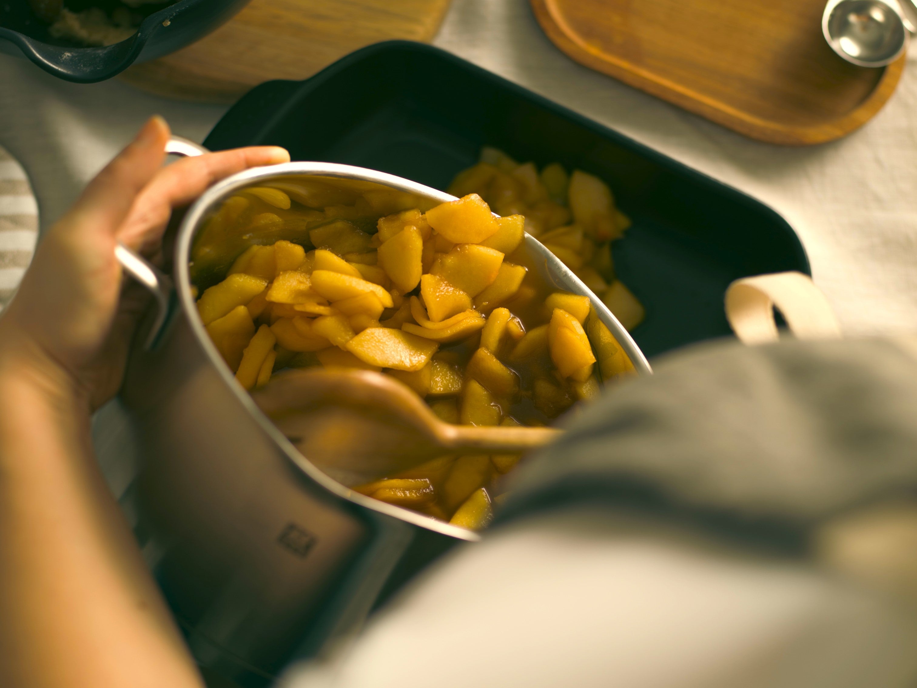 Spooning apples for apple crumble into a saucepan with butter and sugar