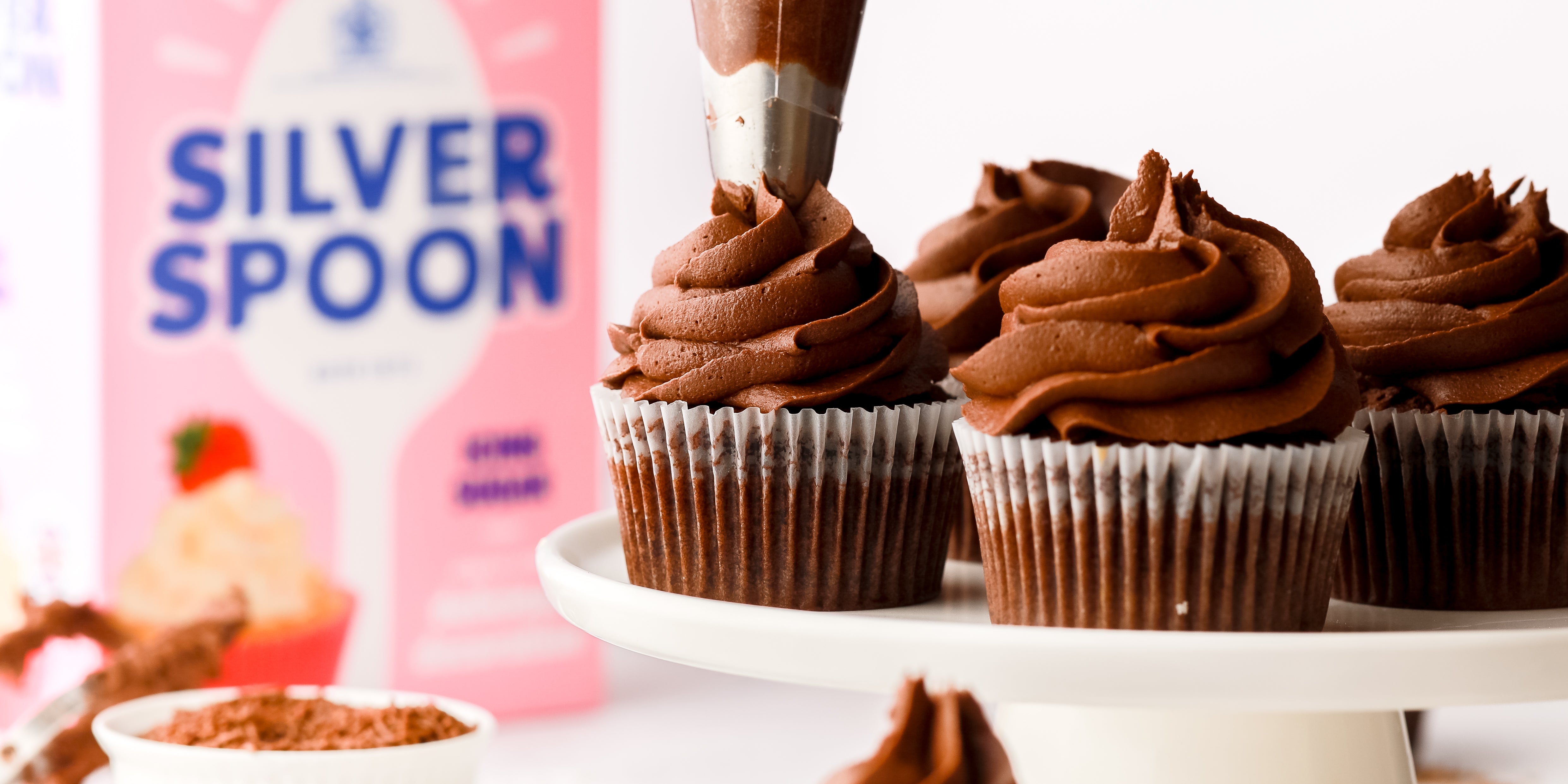 Chocolate buttercream being piped on top of a chocolate cupcake