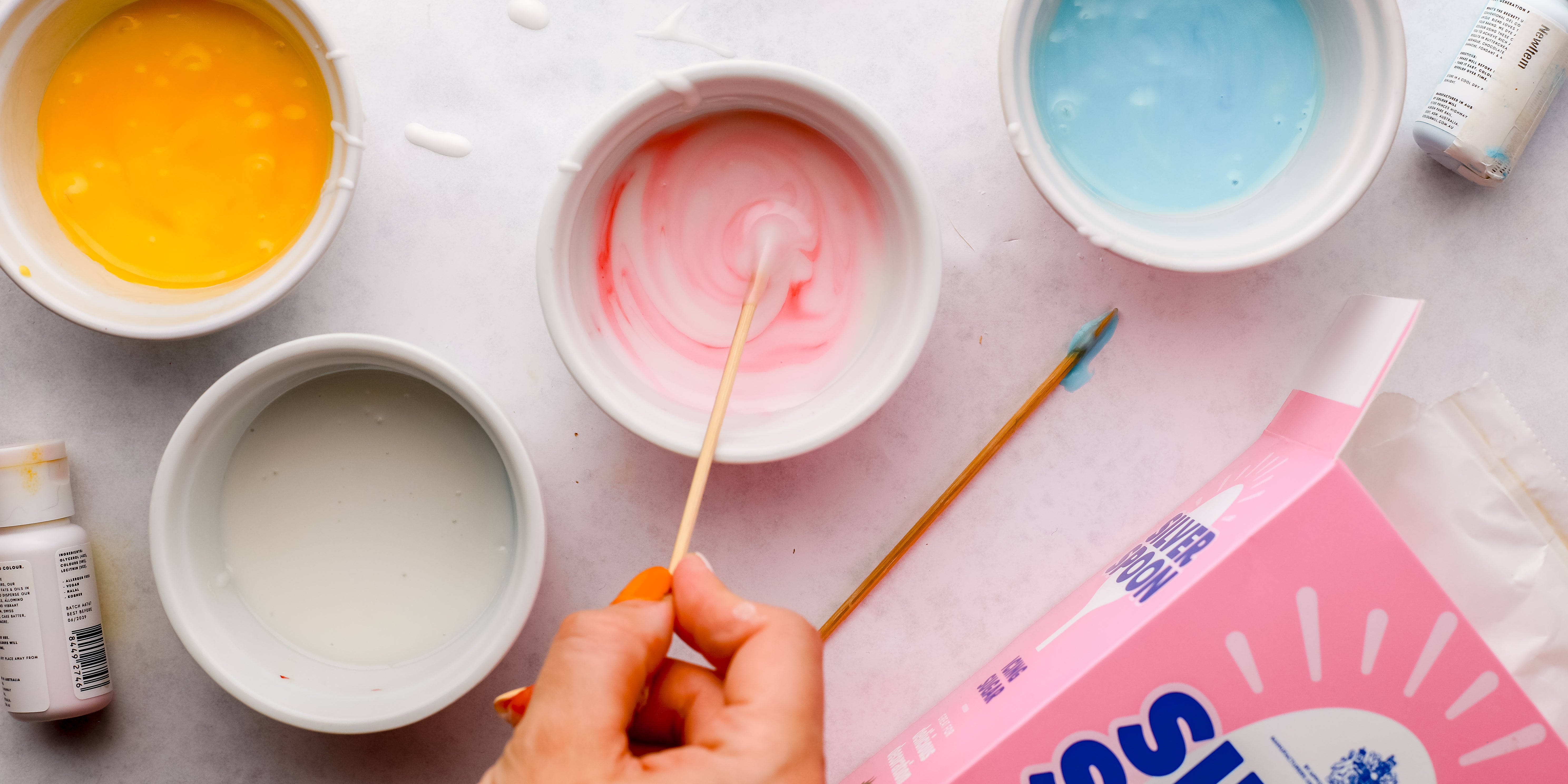 Four bowls of icing being coloured with food dye