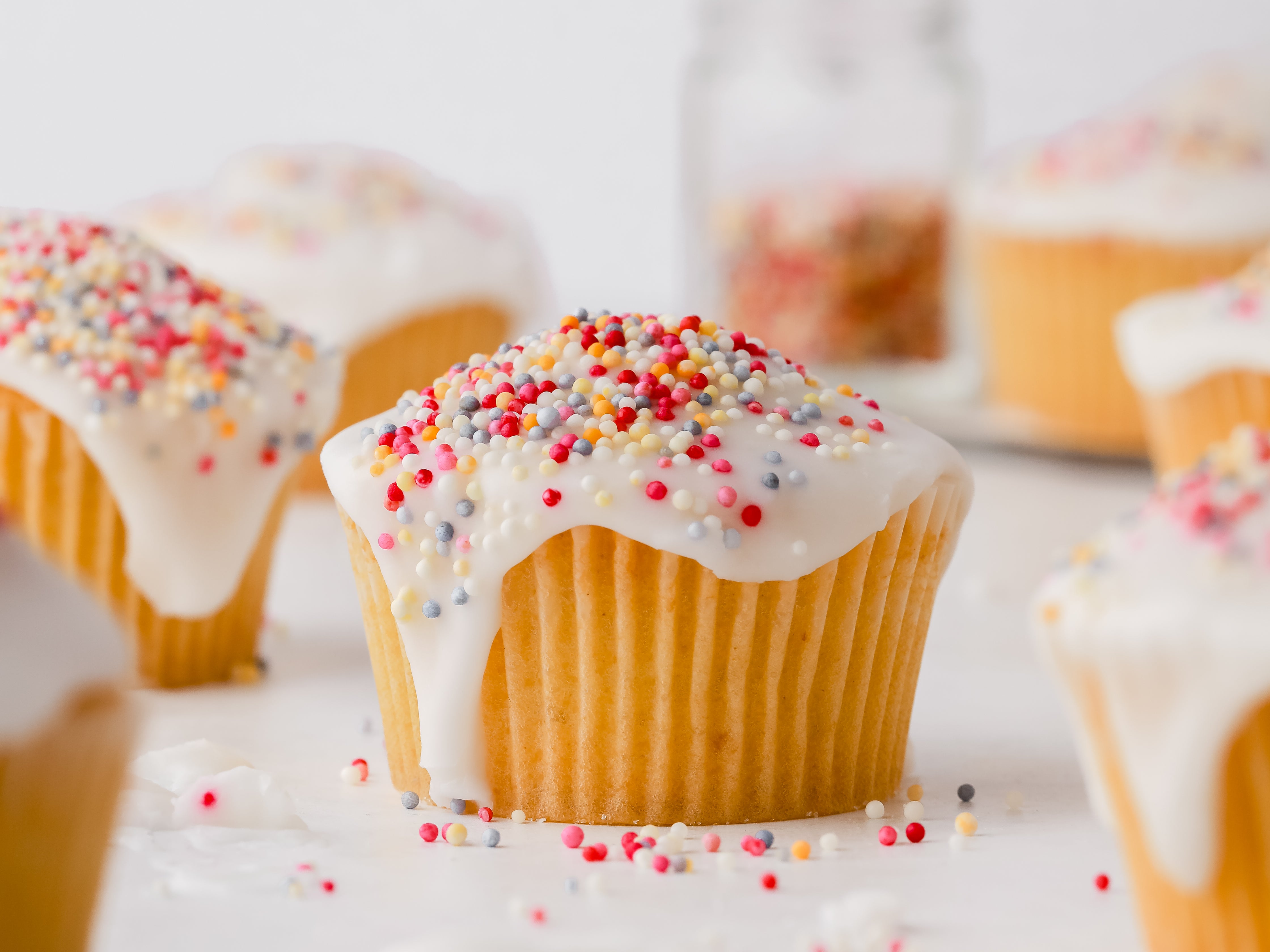 Fairy Cake with white icing dripping down the sides and colourful sprinkled on top