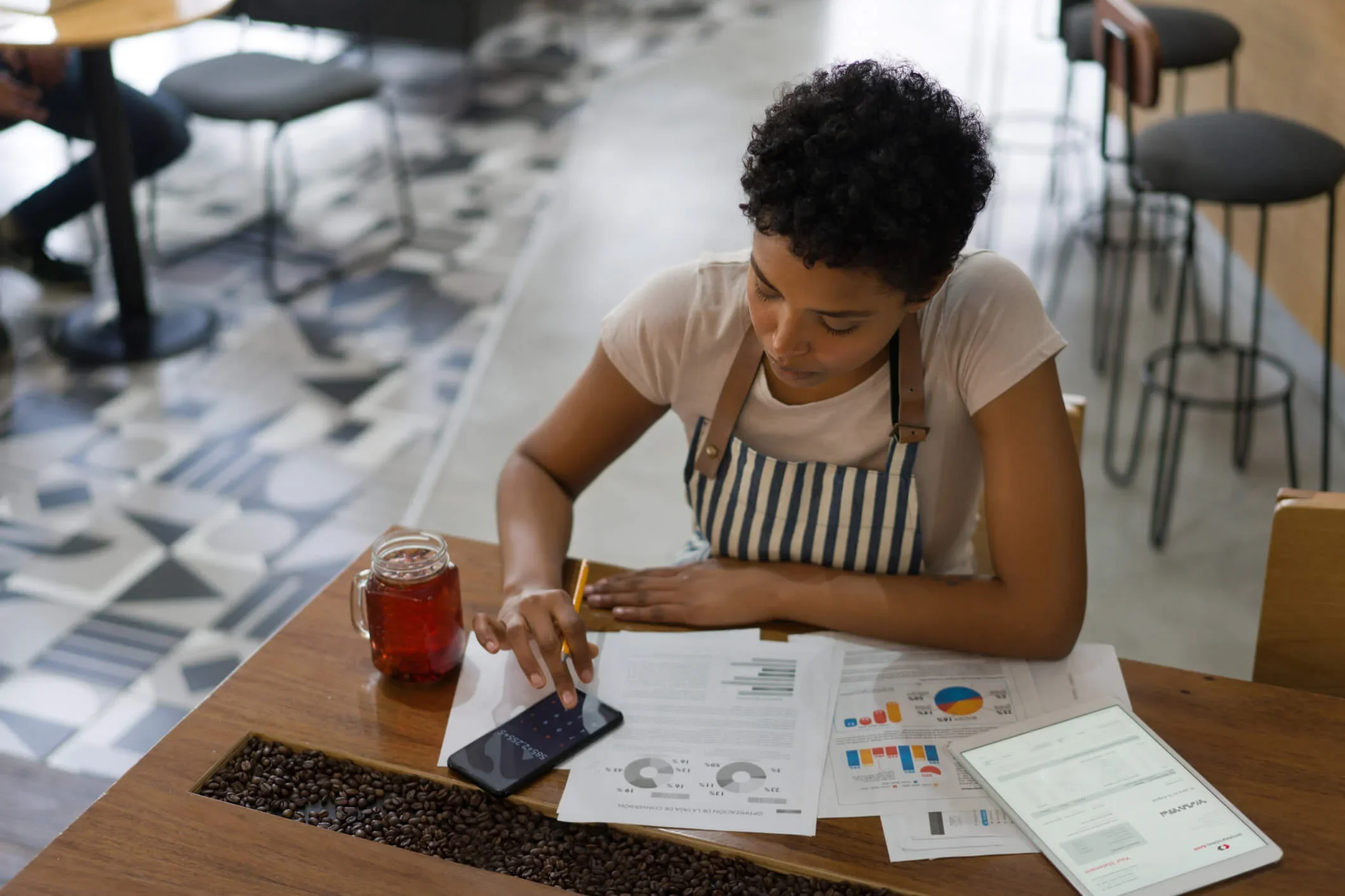 A business owner sits at a table in her shop. she has a calculator and bills on the table and is working out how much VAT she is paying on her business energy bills.