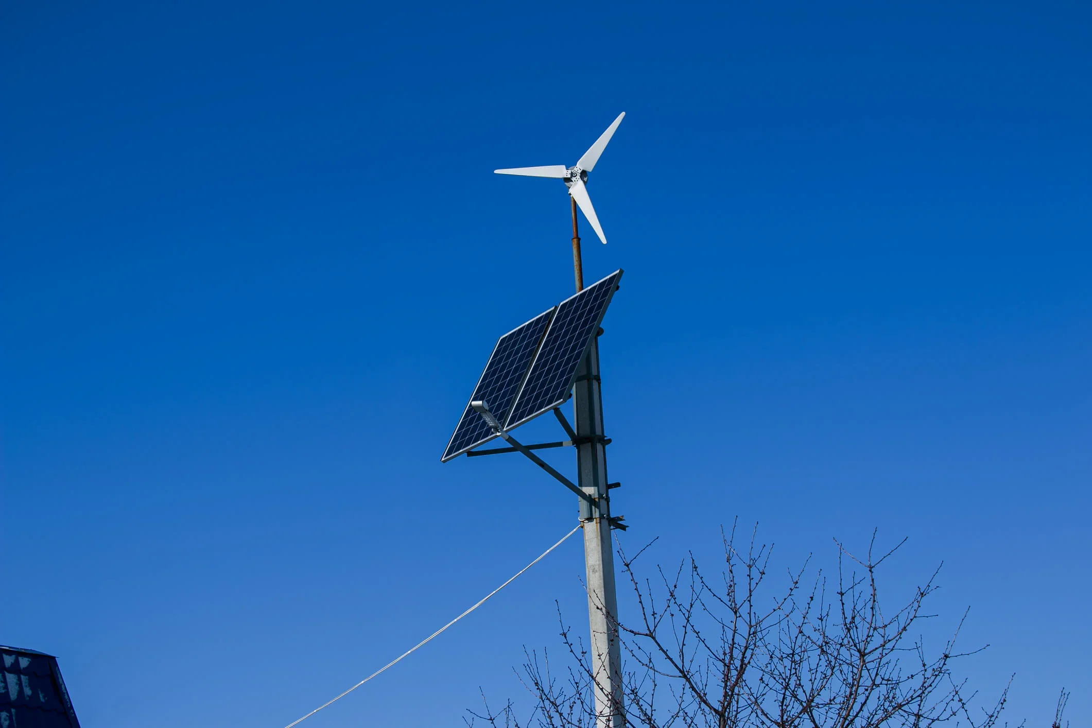 A small wind turbine sits on a pole with an attached solar panel to provide renewable energy to a nearby business.