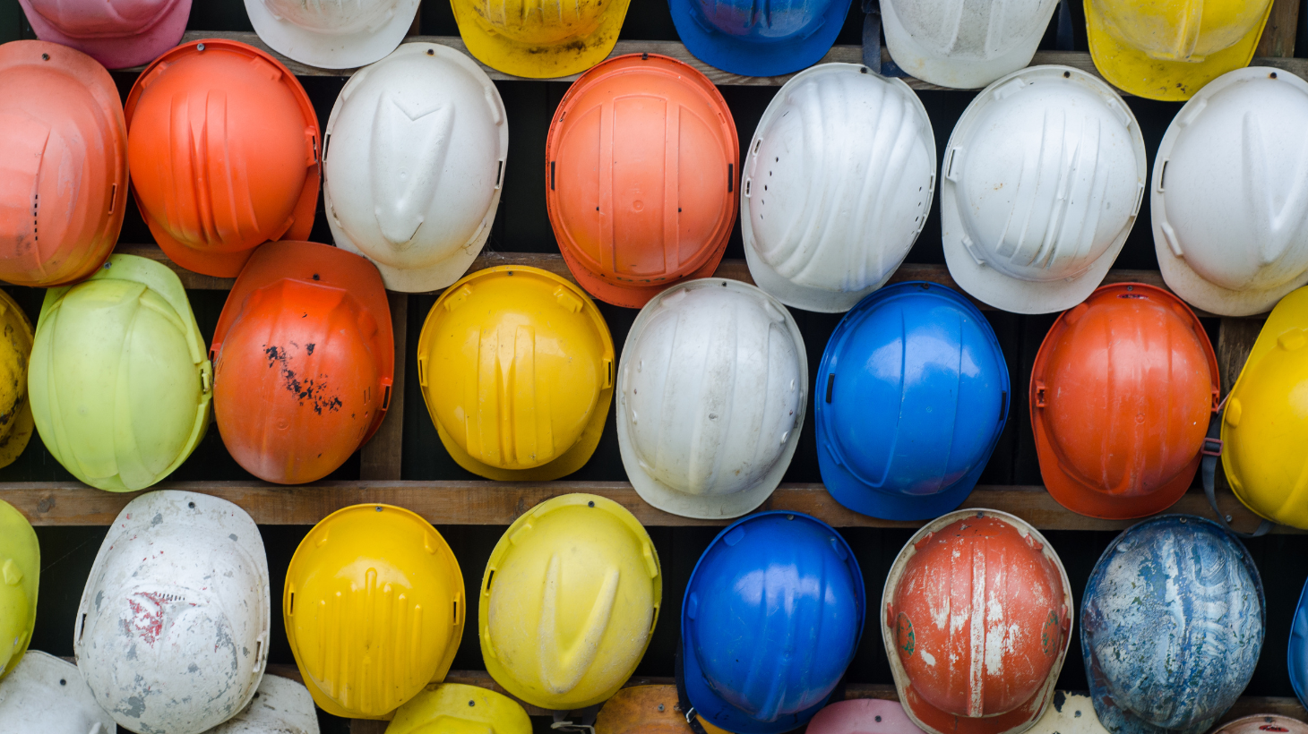 Multi-coloured hard hats stacked in rows.