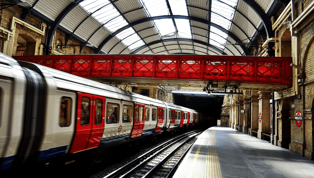 London Underground tube train at a platform with a red footbridge above.