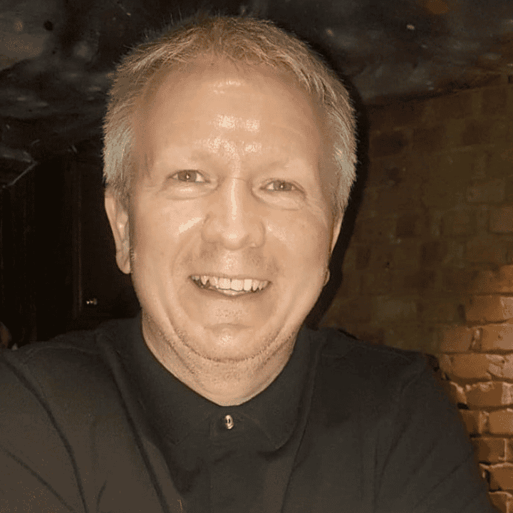 Dean Thwaites, a white man with grey hair in a black shirt and jacket. He is smiling.