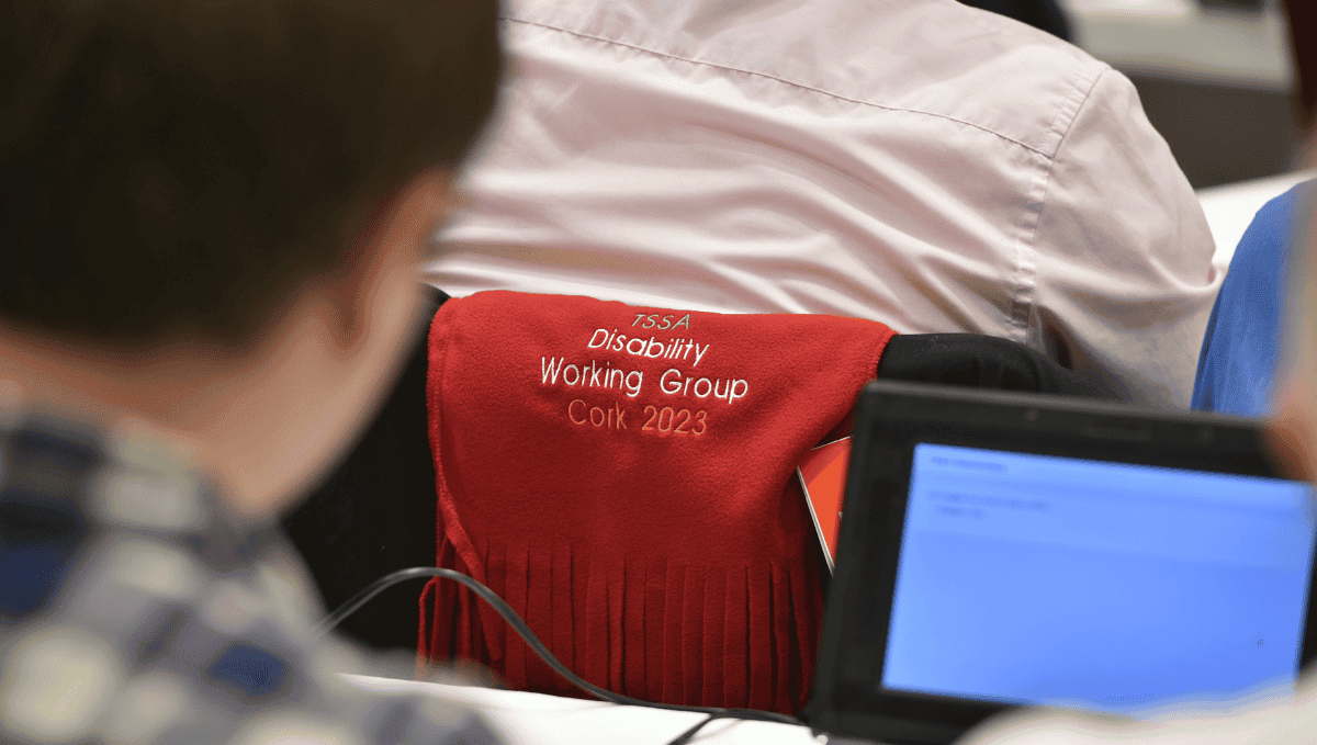 A view over a delegate's shoulder of a flag with the words "Disability Working Group Conference 2023". 