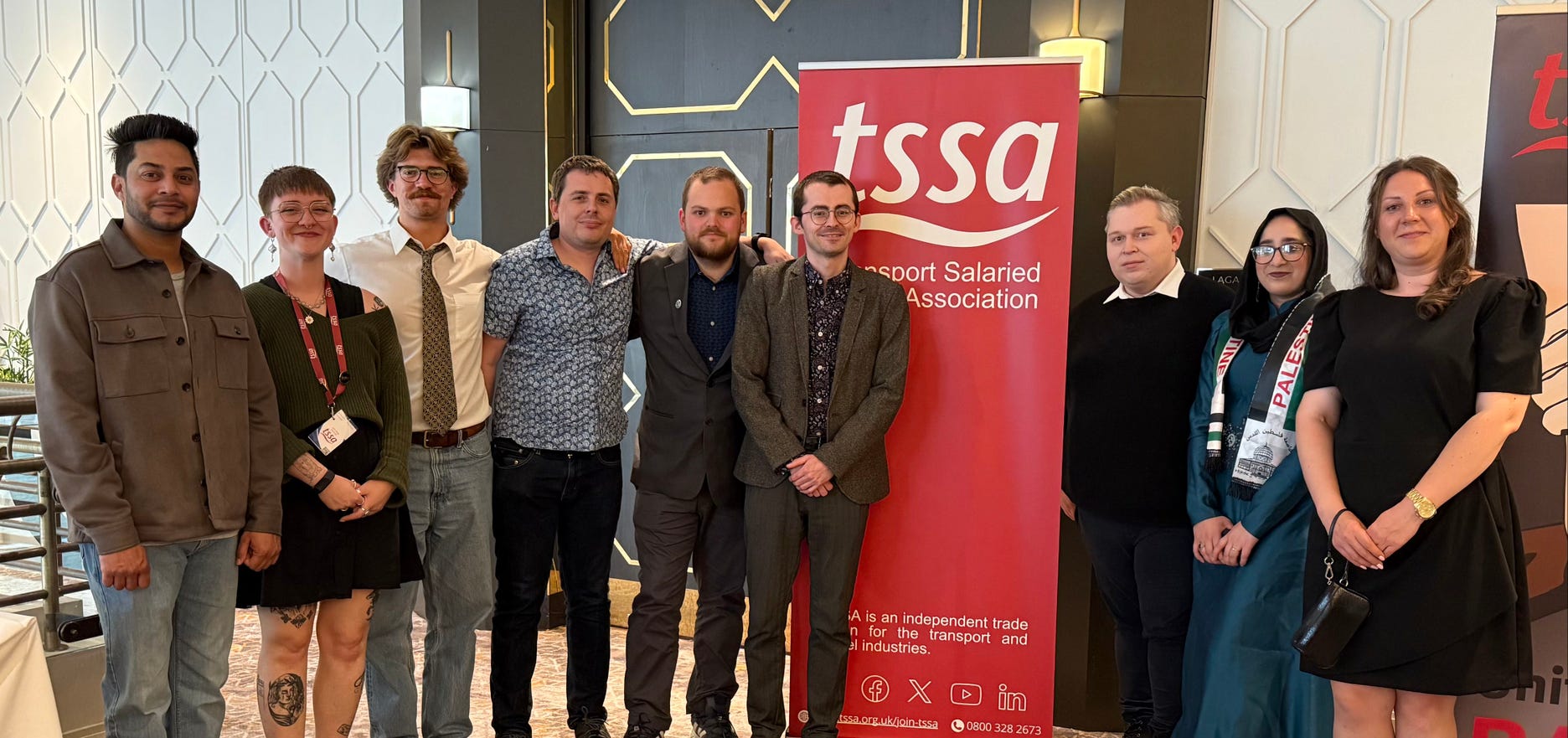 A line of nine young workers standing beside each other with a TSSA red banner behind them.