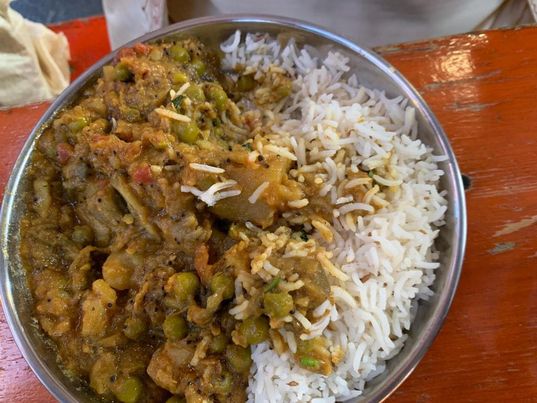 a circular silver plate with rice on the right side and vegetable curry on the left. 