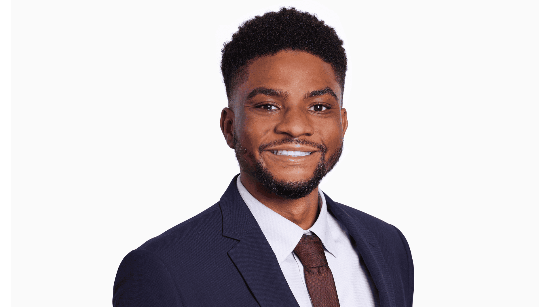 Morrish solicitor, Lawrence Ofori, a black man, smiling at the camera. He wears a smart navy suit with a red tie. He has natural hair with a side fade, a light moustache and a light beard.