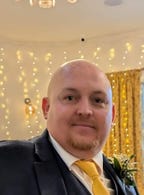 White man in a suit with a ginger blond beard and no hair