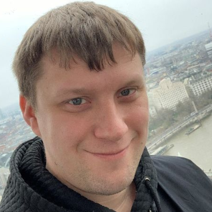 Sam McCully, a white man with brown hair and blue eyes in a dark shirt. He is standing in front of a city skyline and smiling at the camera.
