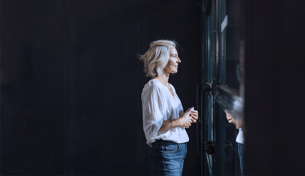 Mustalla taustalla olevassa kuvassa naisoletettu katsoo ulos ikkunasta.