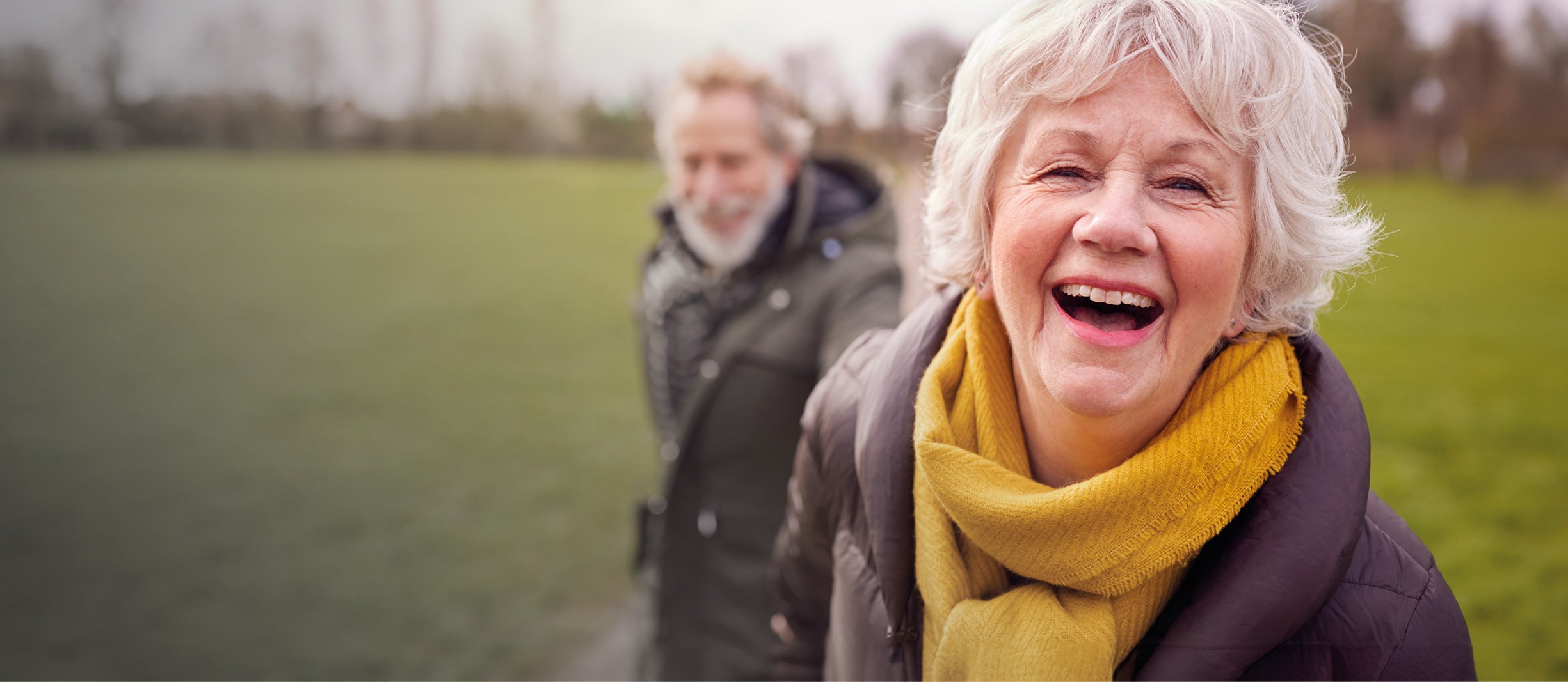Lady leaning forward laughing, holding her husbands hand in the background. 