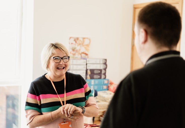 Two people stood talking. You can see the lady is smiling at her colleague, who has his back to the camera.
