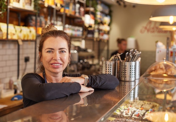 Lady stood at a deli counter smiling.