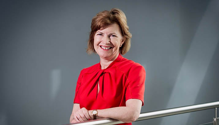 Lucy Winskell stood smiling wearing a red dress with a grey background. 