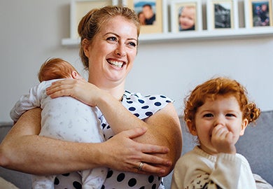A mother holding a baby, sitting on a sofa with a toddler