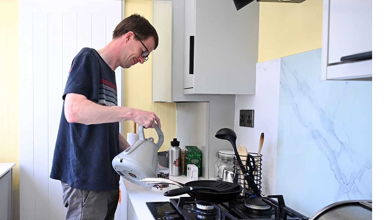 A man making a cup of tea in his kitchen. 