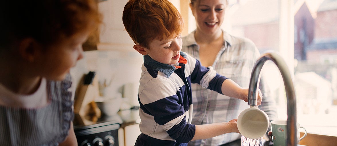 Two children and their mother washing the dishes in the kitchen sink.