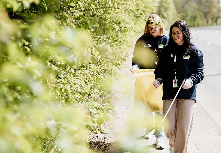 two colleagues litter picking by bushes and trees