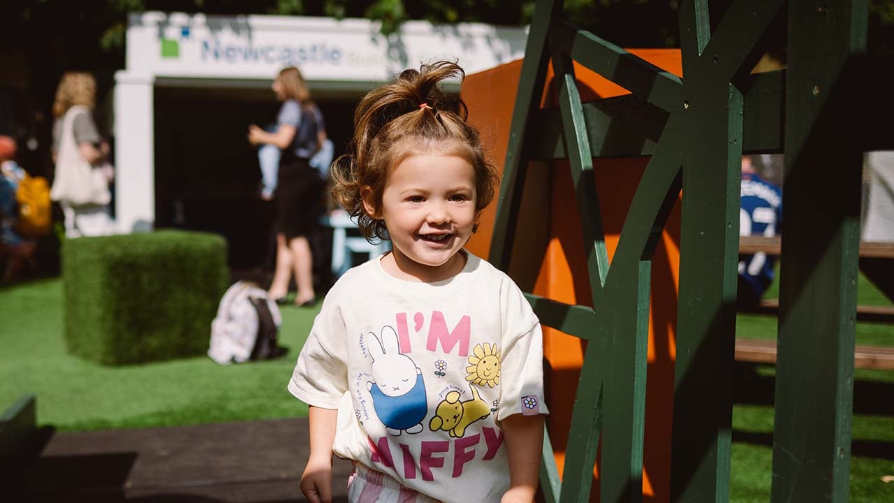 A little girl walking over the bridge smiling, with Newcastle Building Society branch at Tiny Toon in the background. 