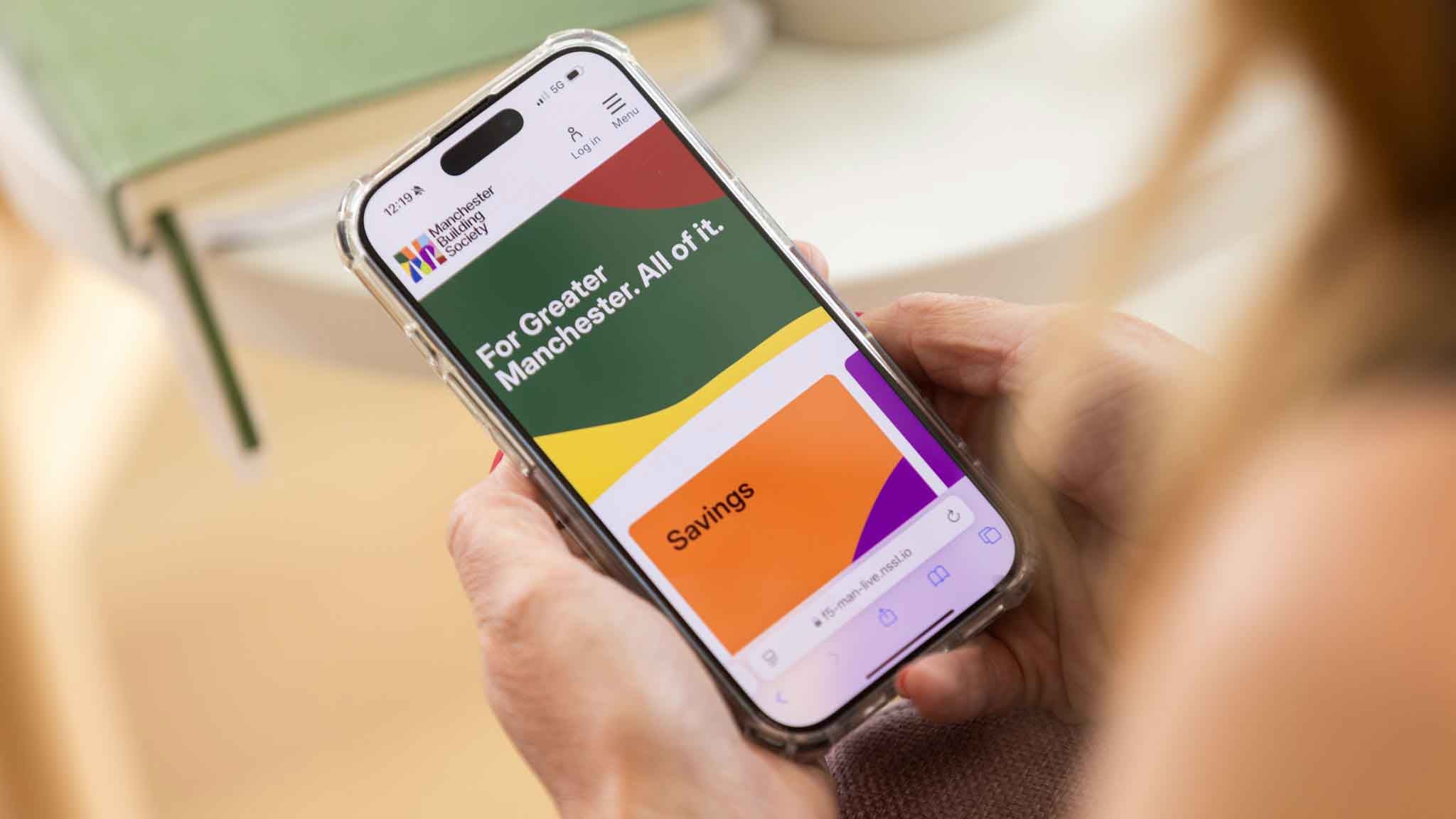 A person holding a mobile phone with the Manchester Building Society website on. 