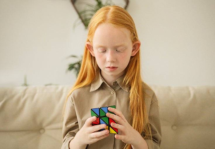 A young girl sits on a sofa and plays with a rubix cube.