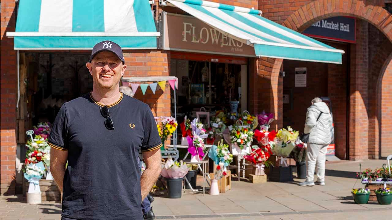 Man stood in front of a flower shop. 